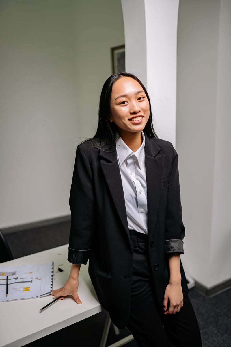 Woman in Black Blazer and Pants Sitting at the Table While Smiling 