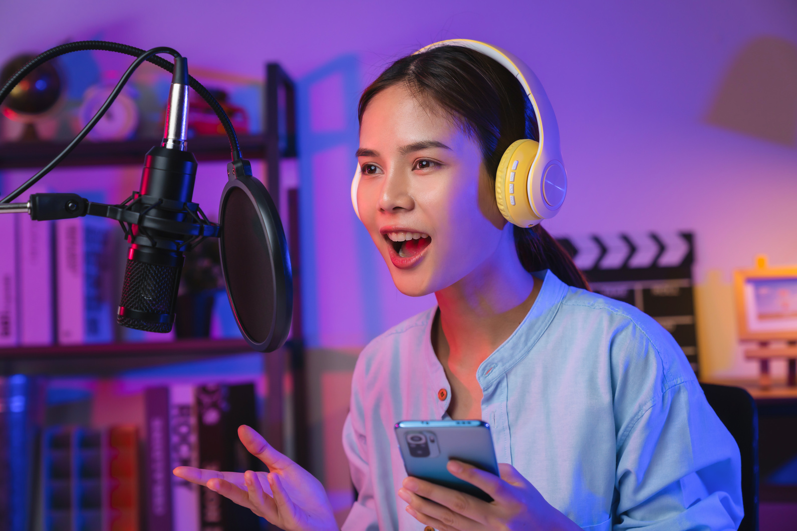 Cheerful beautiful Asian woman wearing headphones and using laptop record podcast at night. Content creator concept.